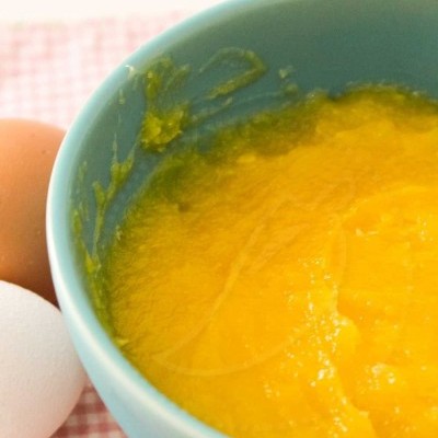 Taça azul com puré amarelo e dois ovos sobre pano xadrez vermelho e branco