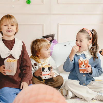 Crianças sentadas com caixas de papel de animais em ambiente decorado com almofadas e balões