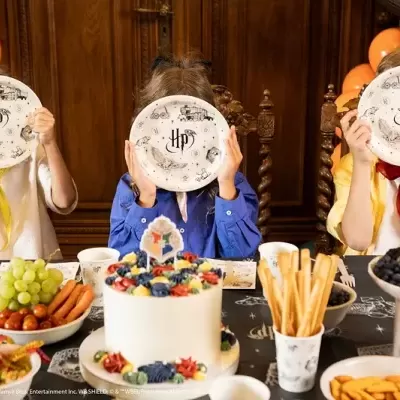 Crianças numa festa com pratos e decoração HP, frutas, bolos e petiscos na mesa