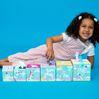 Menina com vestido às riscas rosa e branca com cubos coloridos decorados com unicórnios e animais