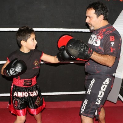 Criança e treinador a treinar boxe num ringue com roupa e luvas de boxe pretas e vermelhas