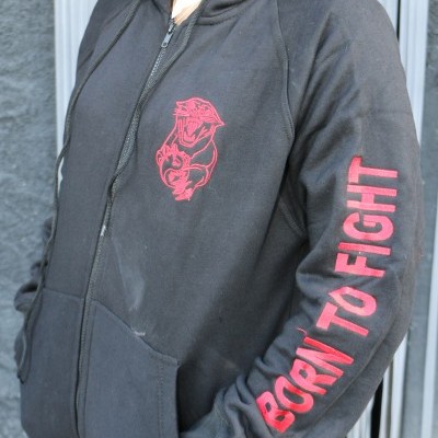 Casaco preto com capuz e fecho, estampa vermelha de criatura e texto BORN TO FIGHT na manga
