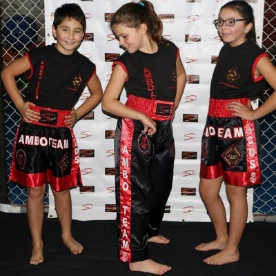 Três crianças com roupas de desporto AMBO TEAM preto e vermelho com detalhes brilhantes