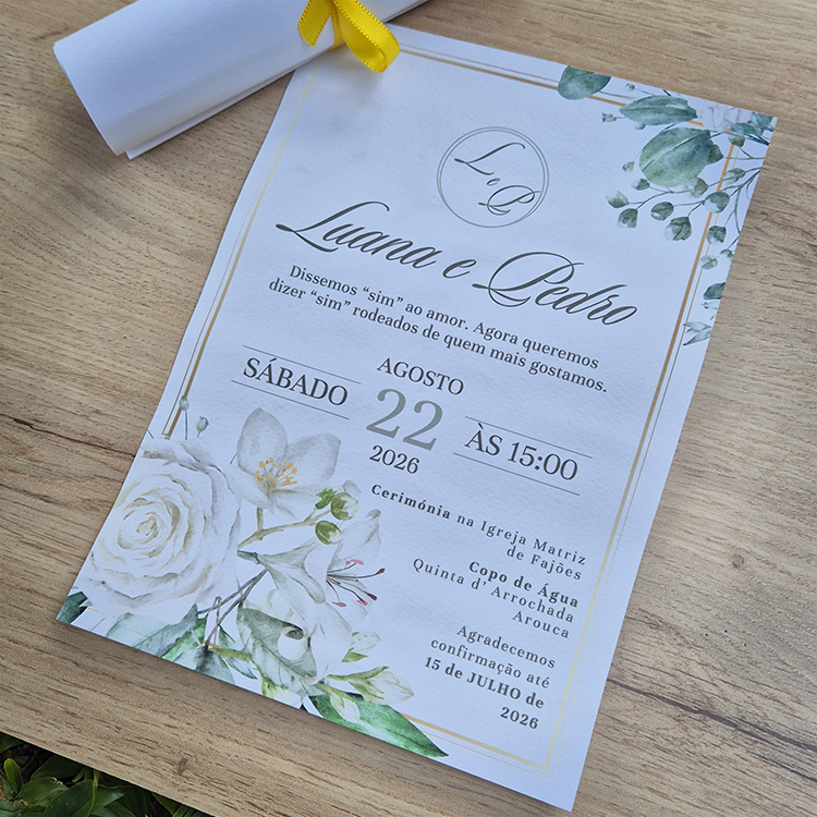 Convite de Casamento Floral Branco Personalizado c/ Laço Convite de casamento com detalhes florais e texto em português sobre mesa de madeira clara.