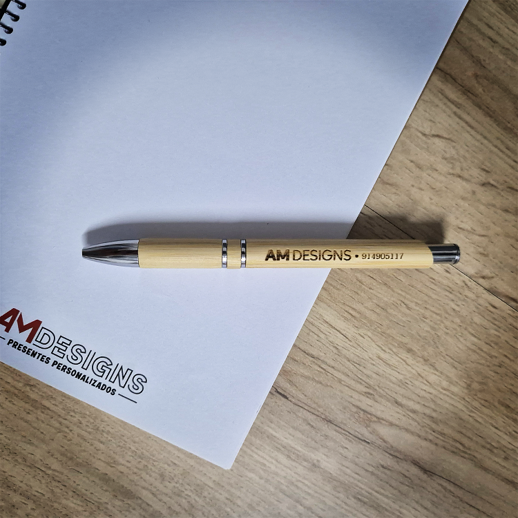 Brinde Empresarial – Caneta Bamboo Premium com Logotipo Caneta com corpo em madeira clara e texto AM DESIGNS e folha branca com logotipo
