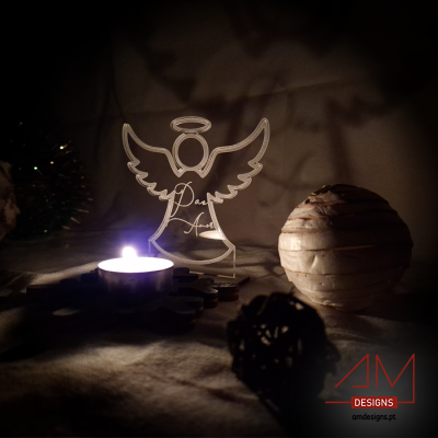 Anjo decorativo em acrílico transparente ao lado de vela acesa e bolas decorativas