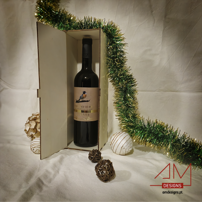 Garrafa de vinho tinto em caixa branca decorada com fita verde metalizada e bolas decorativas, sobre superfície branca