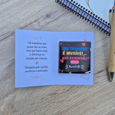 Cartão com mensagem e íman para auxiliar escolar sobre mesa de madeira