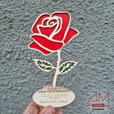 Objeto decorativo de madeira em forma de rosa vermelha com base e texto, parede cinzenta ao fundo