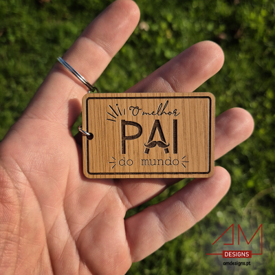Chaveiro em madeira com texto 'O melhor PAI do mundo' numa mão com relva ao fundo
