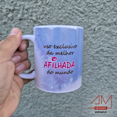 Caneca branca com texto colorido 'uso exclusivo da melhor AFILHADA do mundo' contra fundo cinzento.