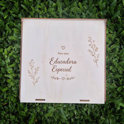 Caixa de madeira clara com texto gravado e desenhos de ramos sobre relva