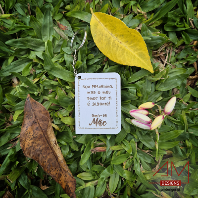 Chaveiro branco com texto em português sobre relva e folhas