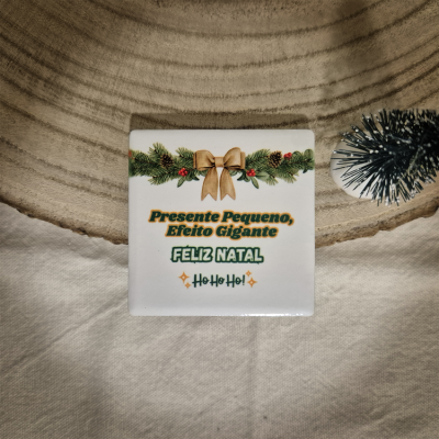 Azulejo decorativo natalício com texto e ramo de pinheiro sobre tecido branco e madeira.