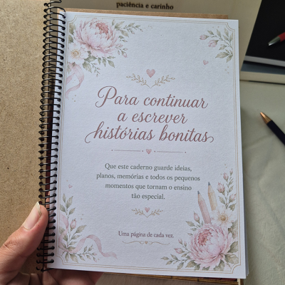 Caderno com capa decorada com flores cor-de-rosa, folhas verdes e texto em português.