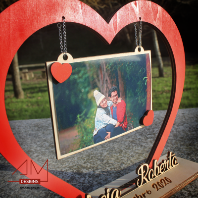 Estrutura de coração vermelho com fotografia pendurada, base com nomes gravados e data.