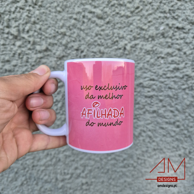 Caneca rosa com texto 'uso exclusivo da melhor AFILHADA do mundo' contra parede cinzenta