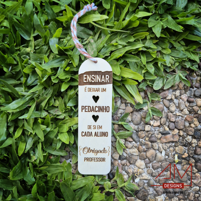 Marcador de livros em madeira com texto em português sobre folhas verdes e pedras pequenas.