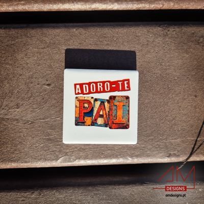 Íman branco com texto colorido 'ADORO-TE PAI' sobre madeira e logotipo AM DESIGNS