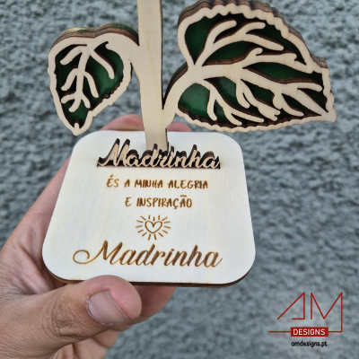 Objeto decorativo de madeira clara com folhas recortadas e texto gravado para madrinha