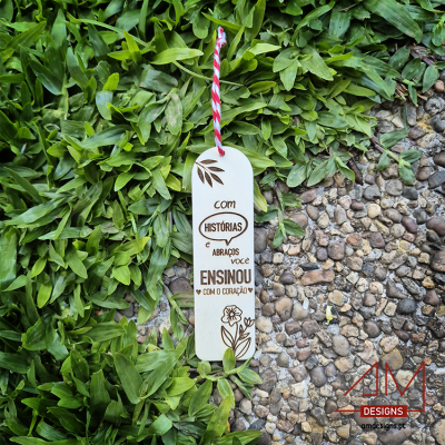 Marcador de página em madeira com cordão, texto e ilustrações, sobre folhas e pedras.