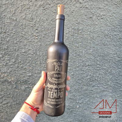 Garrafa preta com texto branco em português e tampa de cortiça, segurada por mão com pulseira vermelha