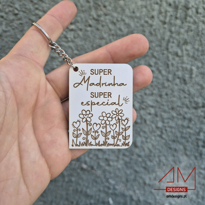 chaveiro branco com texto e flores segurado por mão em fundo de parede cinza