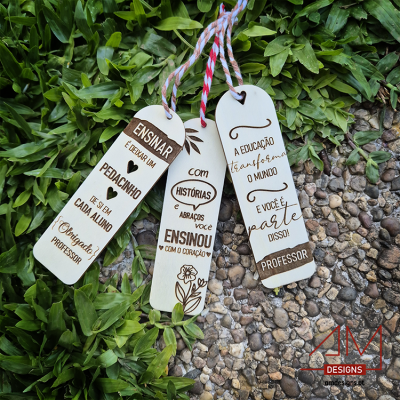 Três marcadores de livros de madeira clara com texto sobre professores, em cima de pedras e folhas