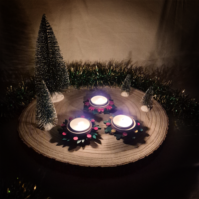 Centro de mesa com velas acesas e pinheiros artificiais sobre base de madeira