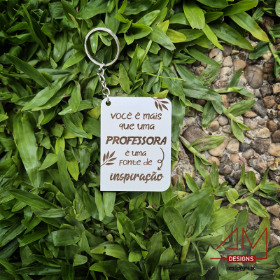 Porta-chaves branco com texto em castanho sobre relva e pedras pequenas.