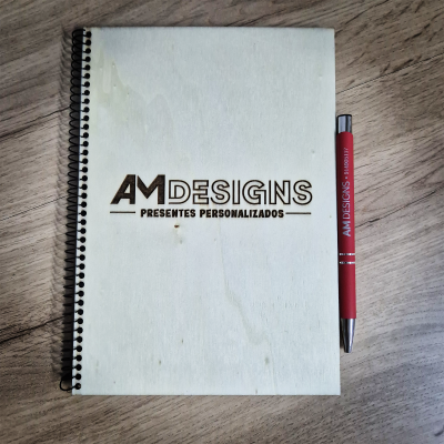 Caderno de madeira com texto AM DESIGNS e caneta vermelha