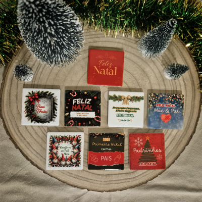 Oito quadrados decorativos de Natal com frases em português, dispostos sobre base de madeira circular com pinheiros artificiais e decoração dourada.