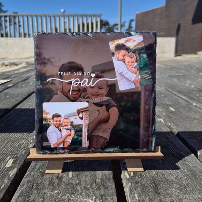 Placa de pedra com fotos e texto Feliz Dia do Pai sobre pequeno cavalete de madeira ao ar livre