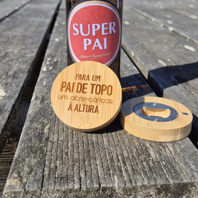 Garrafa de bebida e abre-caricas redondos de madeira com texto gravado sobre mesa de madeira.