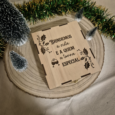 Caixa de madeira decorativa gravada com mensagem de brinde e elementos natalícios ao redor.