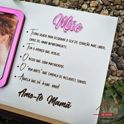Quadro branco decorativo com texto sobre mães em português, com moldura rosa e fundo de pedras.