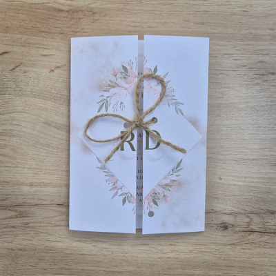 Convite de papel branco com estampas florais e corda rústica sobre madeira