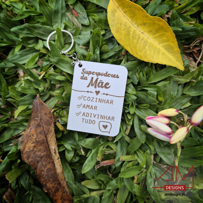 Chaveiro branco com texto 'Superpoderes da Mãe' e tarefas com caixas de seleção sobre relva com folhas secas.