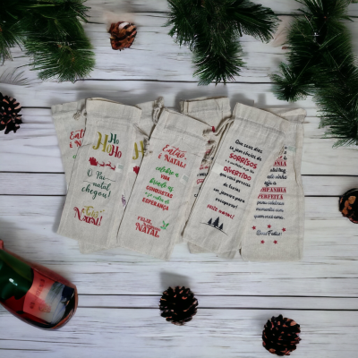 Cinco sacos de tecido com mensagens de Natal em português, decoração natalícia com pinheiros e pinhas, garrafa com rótulo vermelho