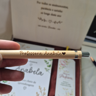 Caneta de madeira clara com gravação personalizada e fundo com papelaria decorativa