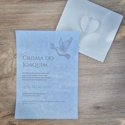 Convite azul claro para Crisma com texto e pomba, envelope branco com fecho de coração sobre mesa de madeira