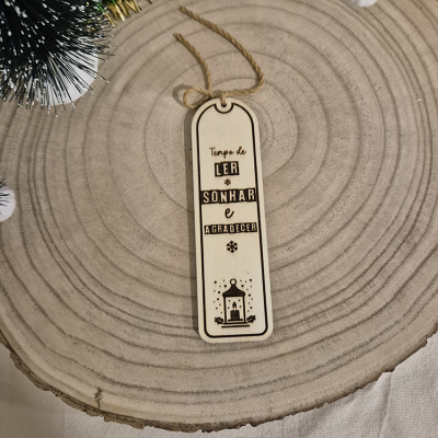 Marcador de livros de madeira clara com frase gravada e cordão sobre tronco de madeira.