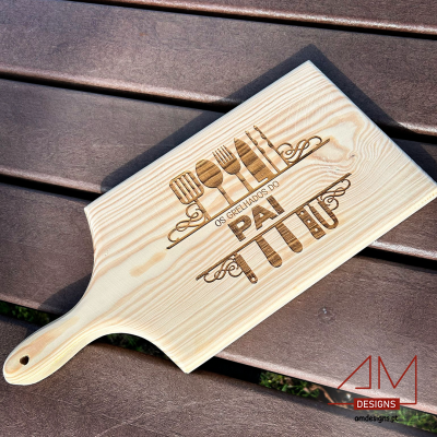 Tábua de madeira clara com gravação de utensílios e texto 'OS GRELHADOS DO PAI'