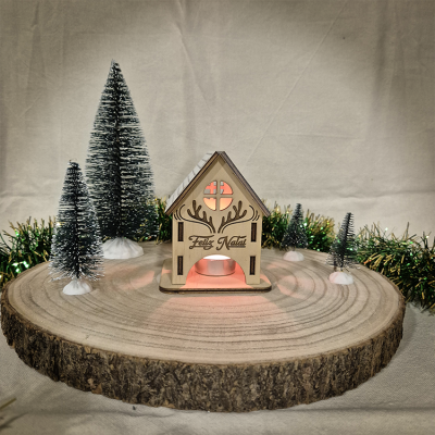 Casa natalícia em madeira com luz e árvores decorativas sobre base de madeira