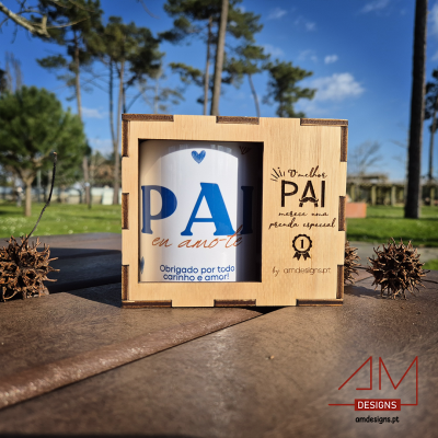 Caneca branca com texto azul em caixa de madeira com inscrições e logótipo AM Designs ao ar livre