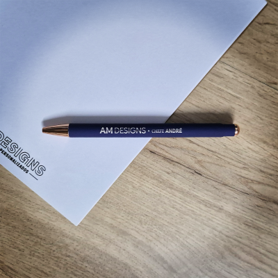 Caneta azul com texto branco e detalhes dourados sobre papel branco e mesa de madeira