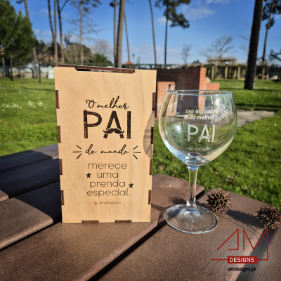 Caixa de madeira com mensagem para o pai e copo de vidro com texto, numa mesa de madeira ao ar livre