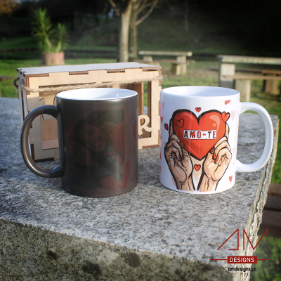 Duas canecas, uma preta e outra branca com desenho de coração vermelho e texto AMO-TE, ao lado caixa de madeira.