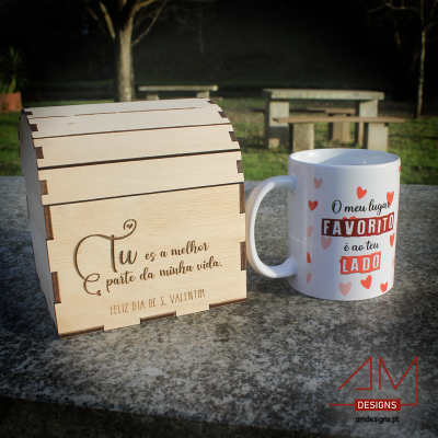 baú de madeira com inscrição de S. Valentim e caneca branca com corações e texto romântico sobre mesa de pedra ao ar livre