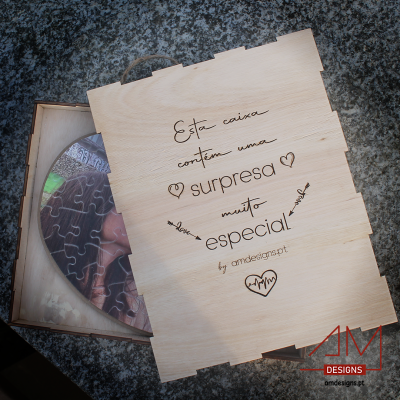 Caixa de madeira clara gravada com texto e logo, contendo um puzzle circular dentro.